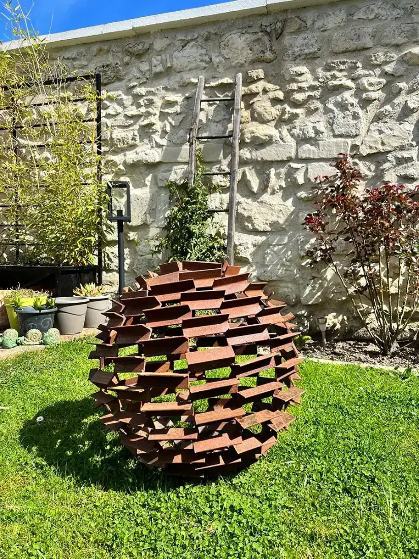 Sculpture sphère en acier massif patiné dans un jardin paysager, pièce signature L'Art de Faire